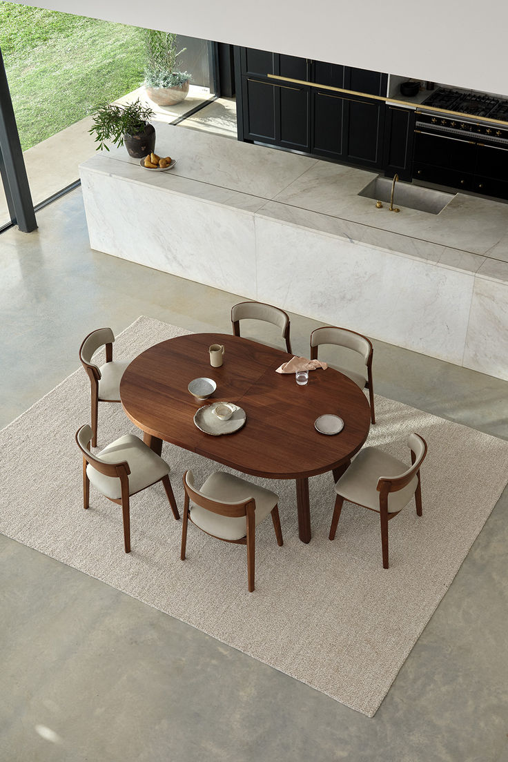 a dining table with six chairs and a rug in front of an open kitchen area