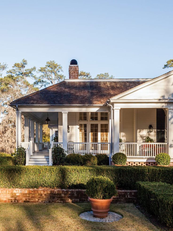 a white house surrounded by hedges and trees with a porch on the second floor that has a large potted planter in front of it