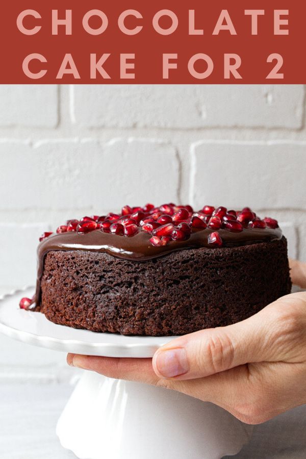 a chocolate cake with pomegranates on top is being held by a person