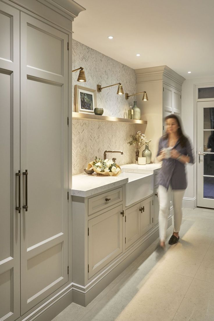 a woman standing in a kitchen next to a sink and cabinets with lights on them