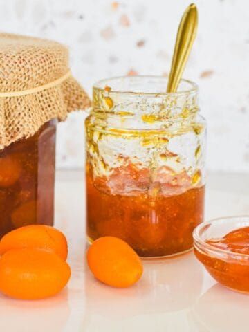 two jars filled with jam and oranges next to each other on a white surface