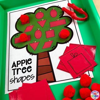 an apple tree shape cutout on a green tray with red pom poms