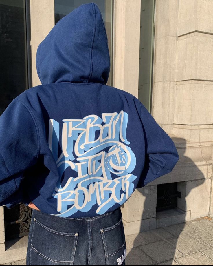 the back of a person wearing a blue hoodie with graffiti on it's chest