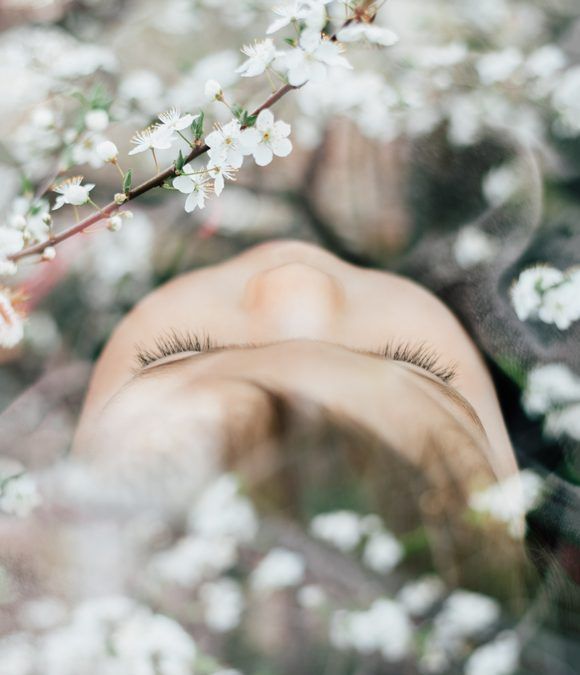 a woman's eyes are seen through the branches of white flowers in front of her