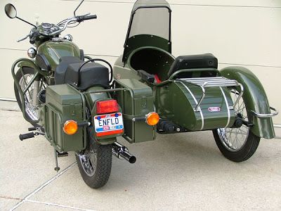 a green motorcycle parked next to a white building with a side car on the back