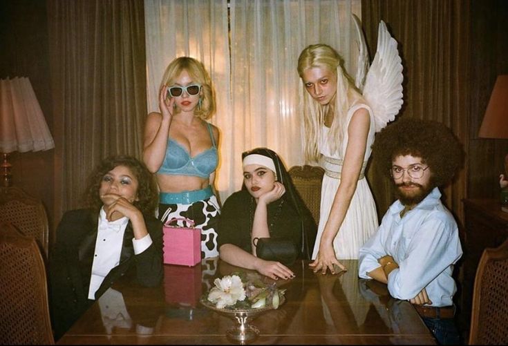 a group of people sitting around a table with one woman dressed like an angel and the other as a man