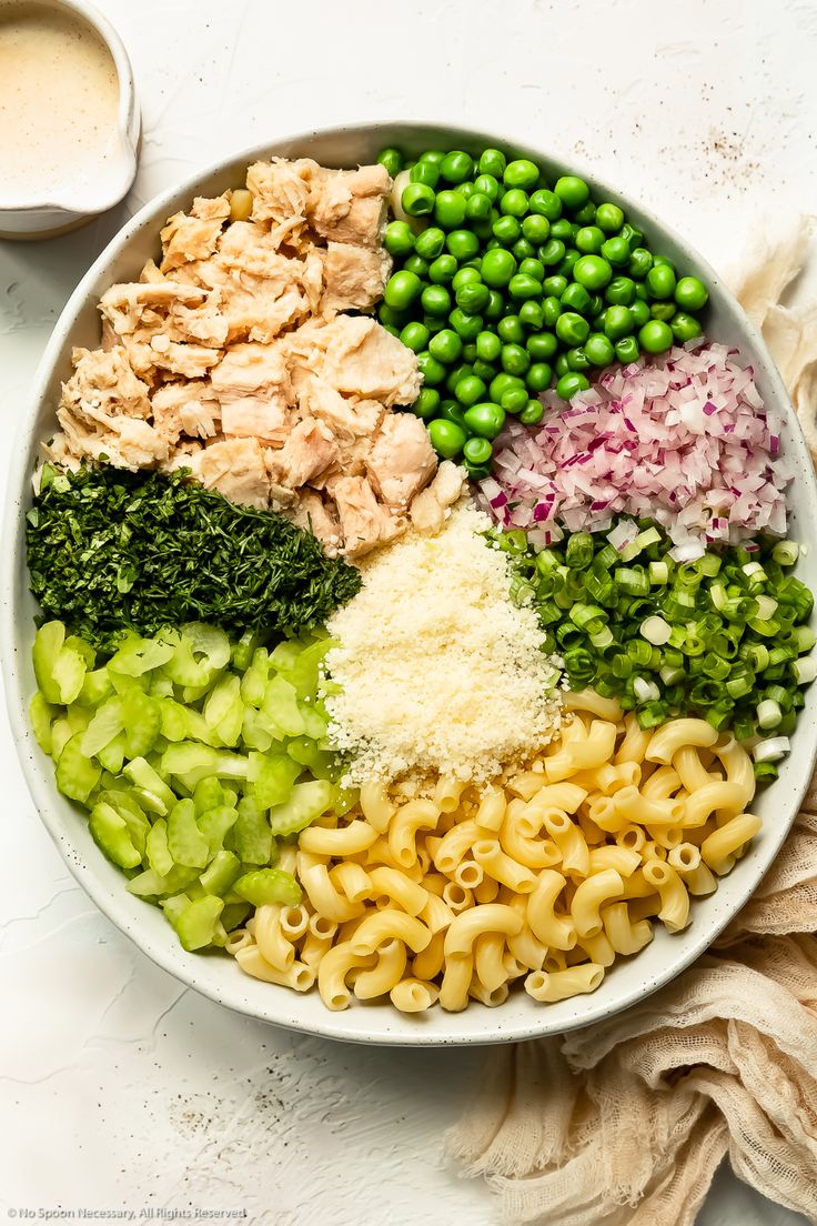 a bowl filled with pasta, peas, and meats next to a cup of sauce