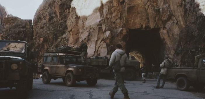 two men are walking in front of jeeps that are parked near a rocky mountain