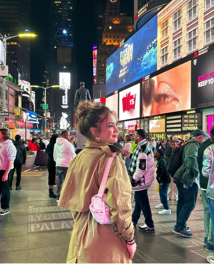 a woman is standing in the middle of a busy city street at night with people walking around