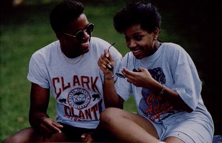 two people sitting on the ground laughing and looking at their cell phones