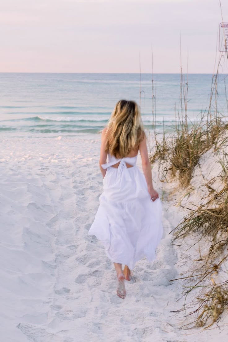 a woman in a white dress walking on the beach