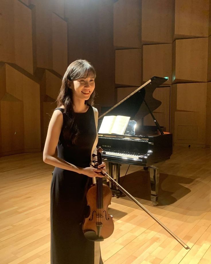 a woman holding a violin in front of a piano