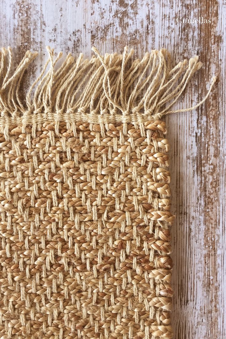 a piece of woven material with fringes on top of it, sitting on a wooden surface