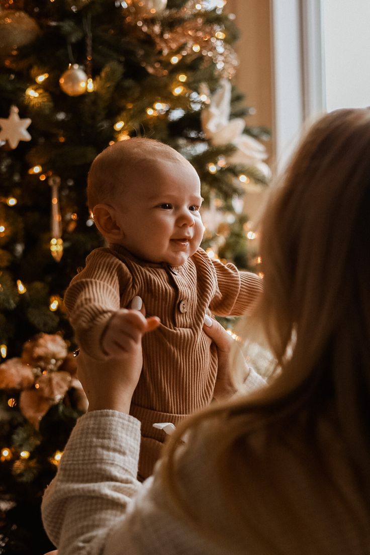 a woman holding a baby in front of a christmas tree