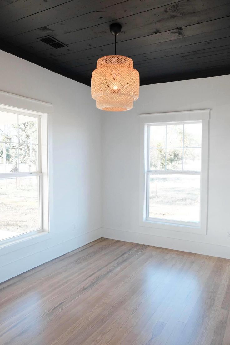 an empty room with two windows and a light fixture hanging from the ceiling above it