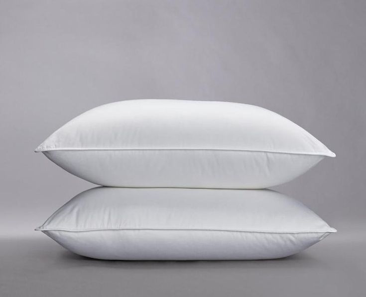 two white pillows stacked on top of each other in front of a gray background,