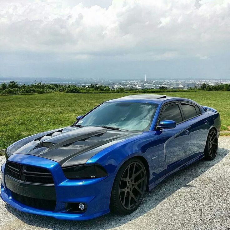 a blue dodge charger parked on top of a parking lot next to a field