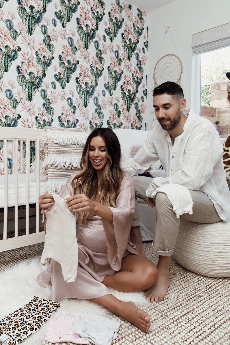 a man and woman sitting on the floor next to a baby crib holding clothes