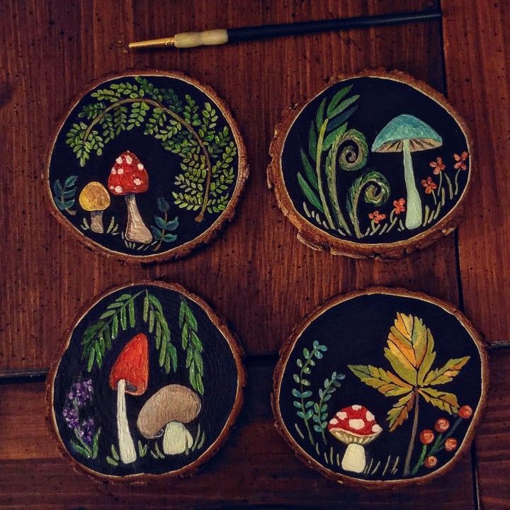 four painted wooden slices with mushrooms and plants on them, sitting on top of a table