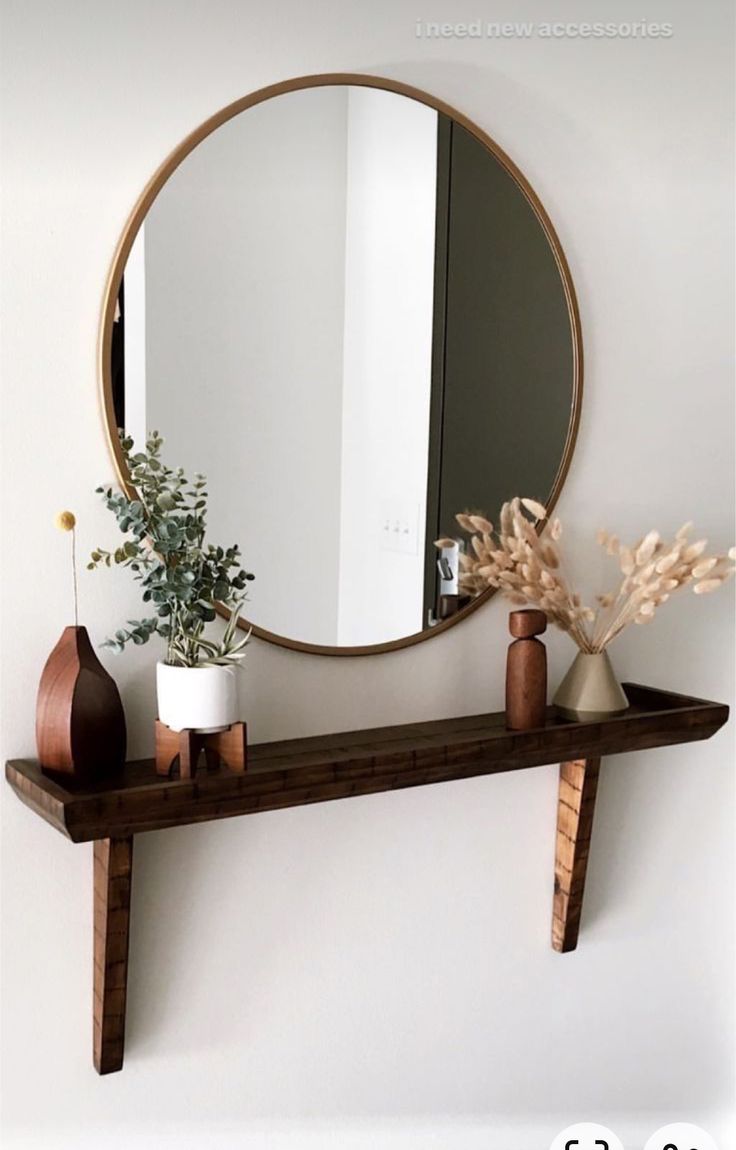 there is a mirror and vase on the shelf in front of the mirror with plants