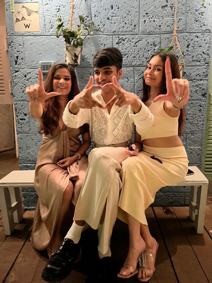 three people sitting on a bench making the peace sign with their hands while one woman holds her hand up