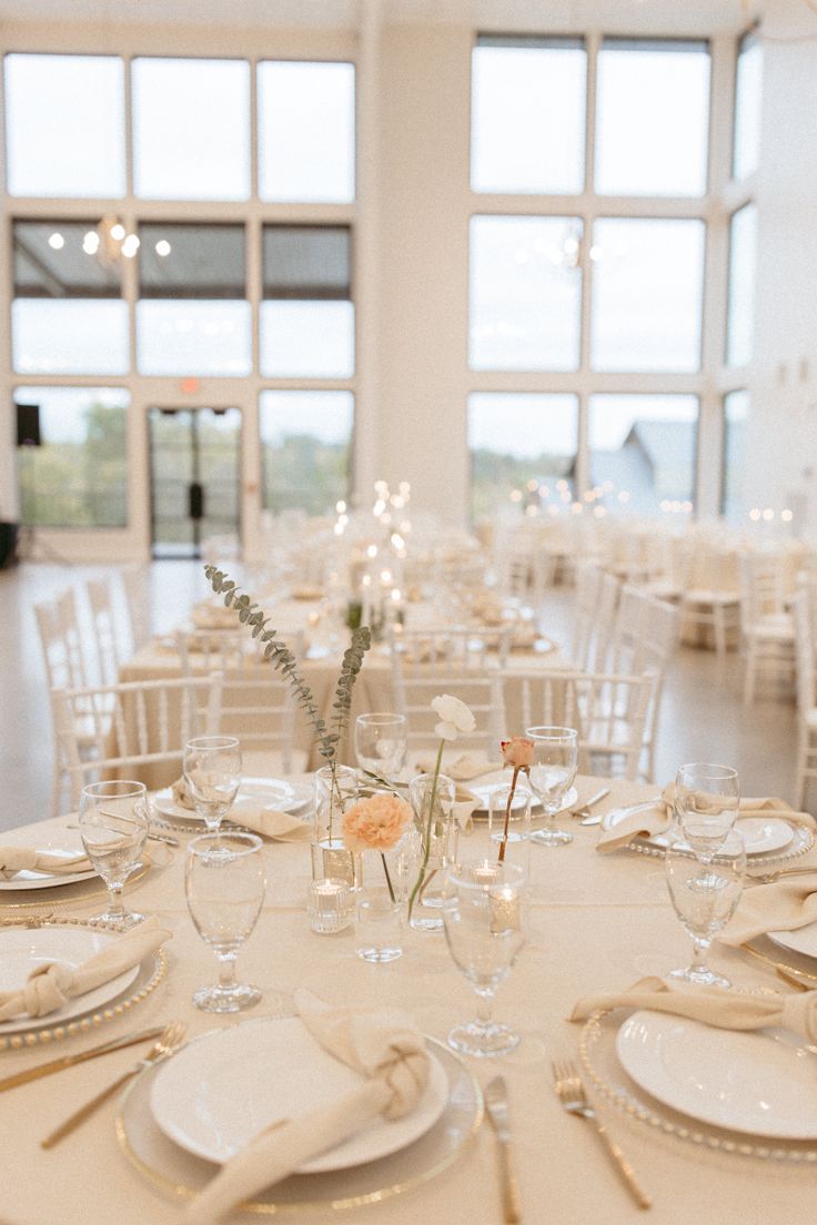 the tables are set with white plates and place settings for an elegant wedding reception in front of large windows