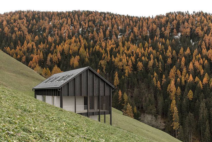 a small house on the side of a hill with lots of trees in the background