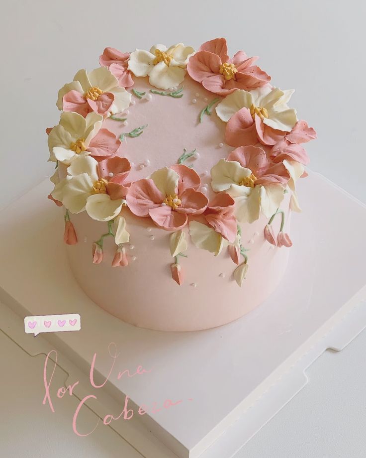 a pink cake with white and yellow flowers on top is sitting on a card board