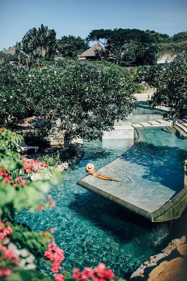 an outdoor swimming pool surrounded by greenery and trees with a person floating in it