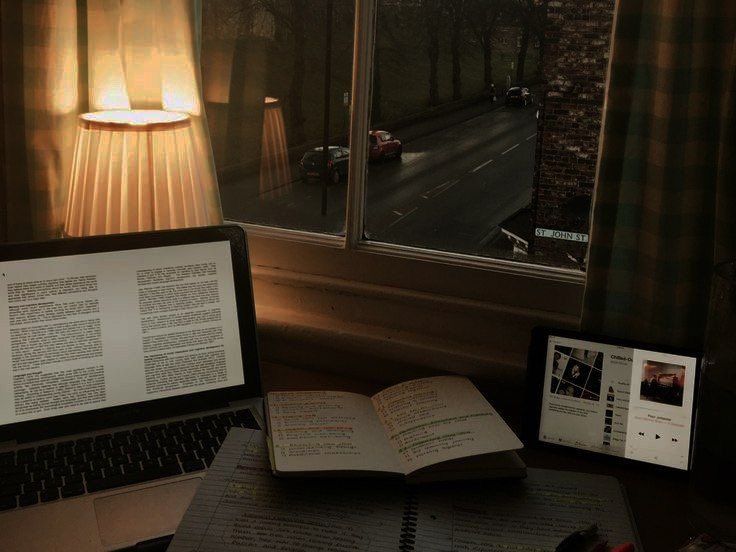 an open book sitting on top of a desk next to a laptop computer and lamp