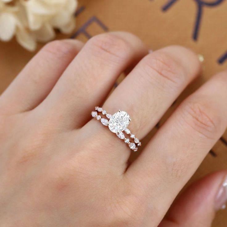 a woman's hand with a diamond ring on top of her finger, next to a flower