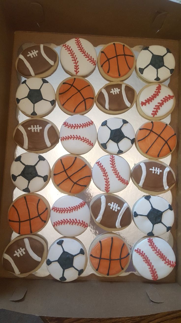 decorated cookies in the shape of sports balls are displayed on a cardboard box, ready to be eaten