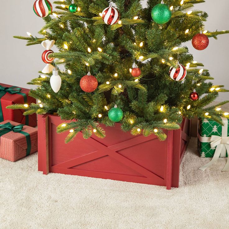 a small christmas tree in a red wooden crate with ornaments on it and presents underneath