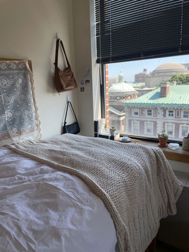 a bed with white sheets and pillows in a bedroom next to a window overlooking the city