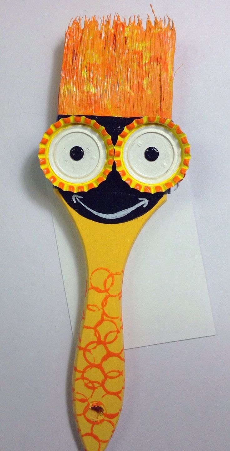 an orange and yellow brush with googly eyes on it's head, sitting on top of a piece of paper