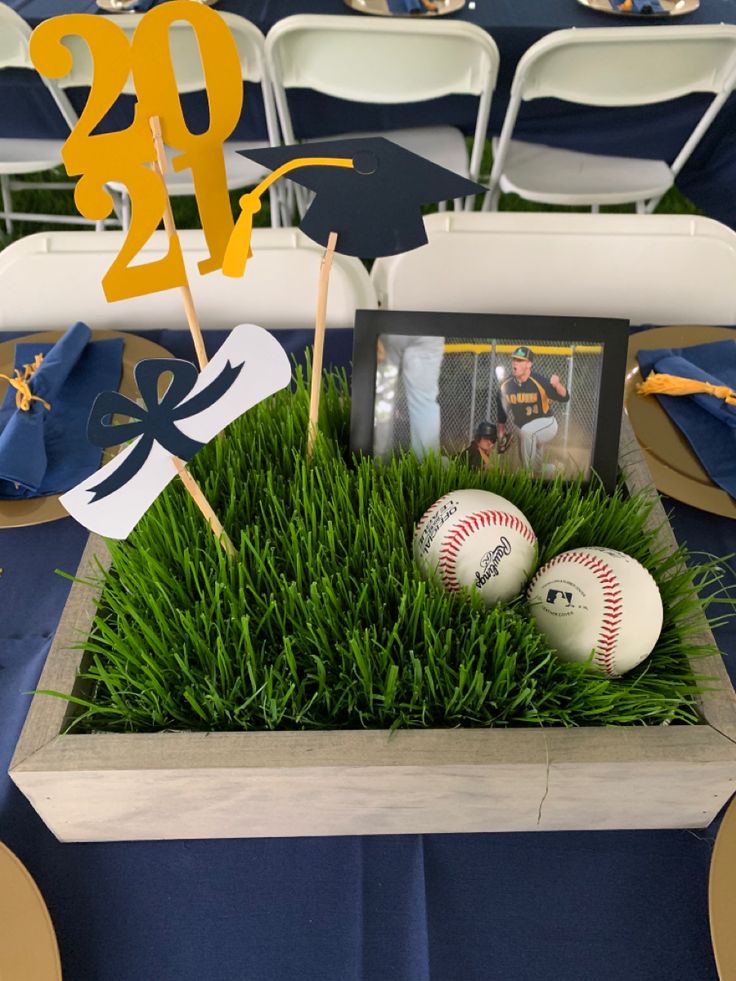 two baseballs are sitting in the center of a table with grass and decorations on it