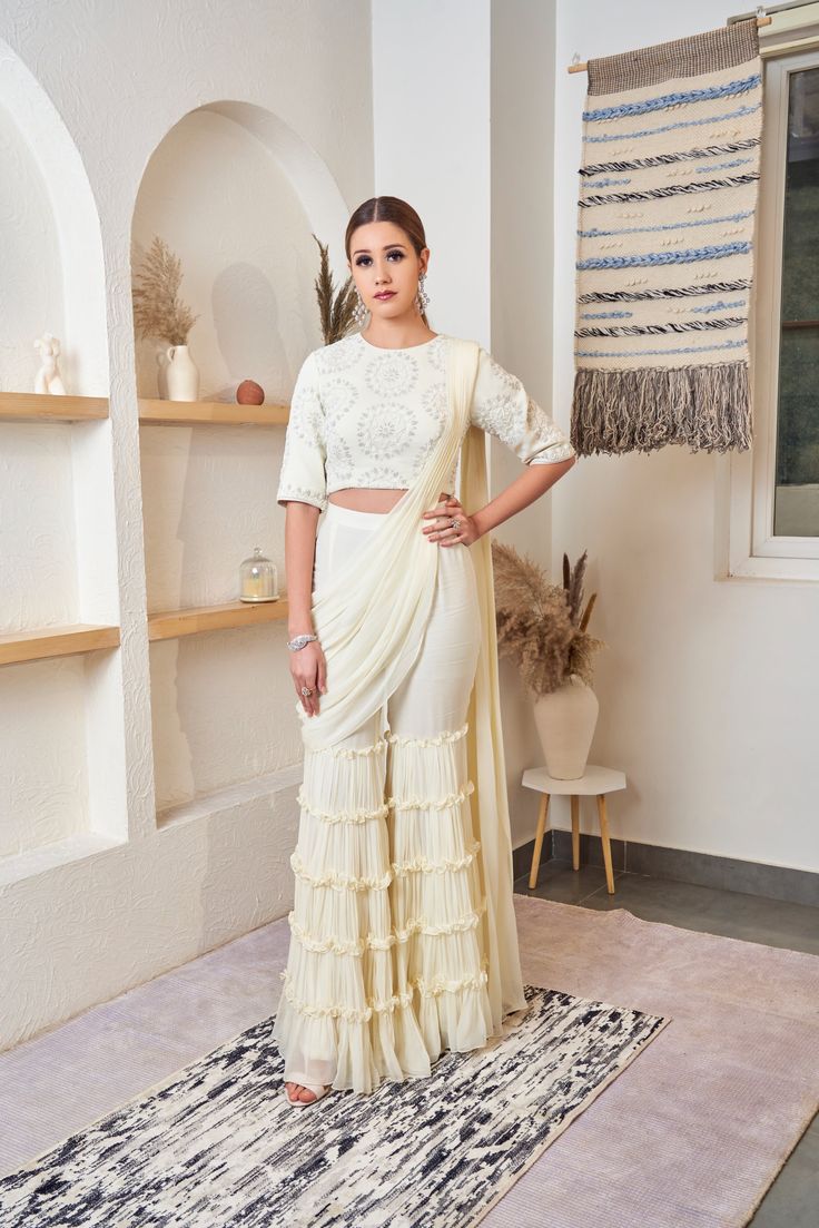 The off-white Sharara saree is made of georgette. The ensemble is etched with frills and scintillating details, it radiates elegance and class. Delivery Period: 2-3 weeks White Fitted Pre-draped Saree For Eid, Bollywood Style Palazzo Set With Ruffles In Georgette, Off White Traditional Drape Blouse Piece For Reception, Off White Blouse Piece For Reception With Traditional Drape, White Bollywood Pre-draped Saree For Reception, Traditional Ruffled Palazzo Set For Wedding, Traditional Wedding Palazzo Set With Ruffles, Festive White Pre-draped Saree With Unstitched Blouse, Designer Pre-draped Off White Saree With Sheer Dupatta