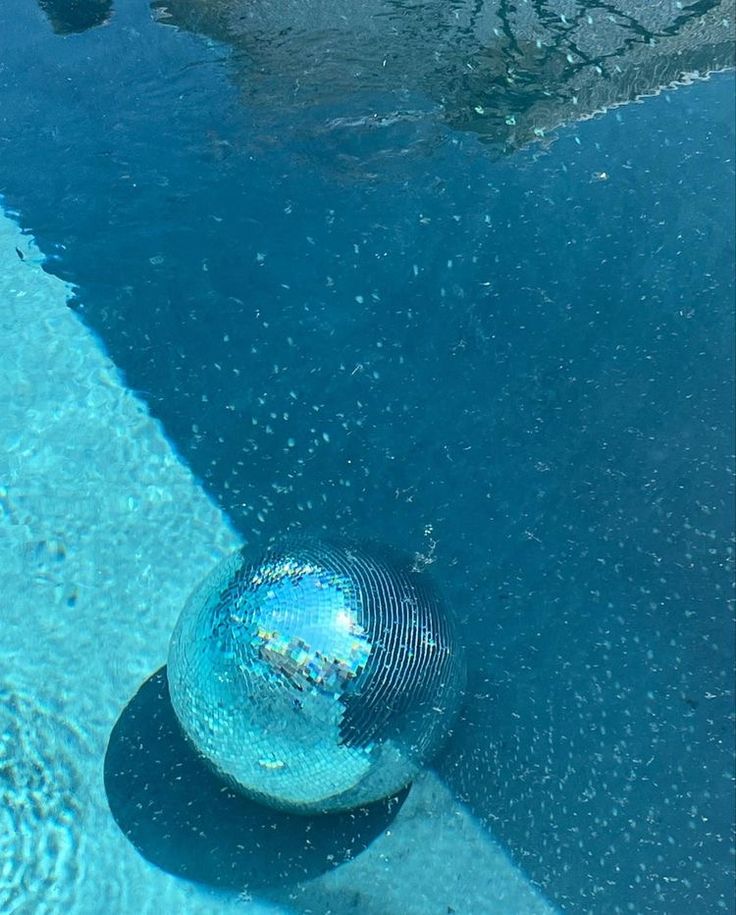 a shiny ball floating in the water next to a swimming pool with no people on it