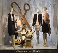 mannequins dressed in black and white clothing with large wooden scissors on display