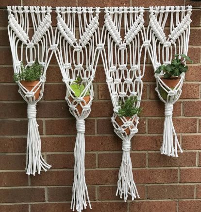 four white macrame plant hangers with plants in them on a brick wall