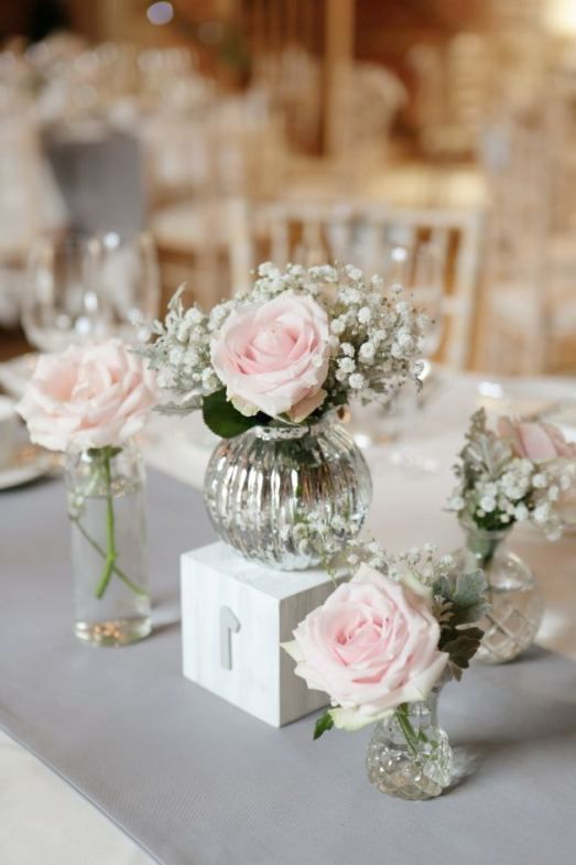 three vases filled with pink roses sitting on top of a white tablecloth covered table