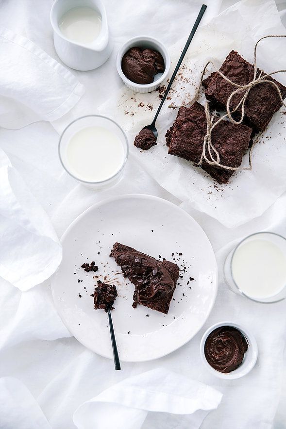 two pieces of chocolate cake on plates next to cups of milk