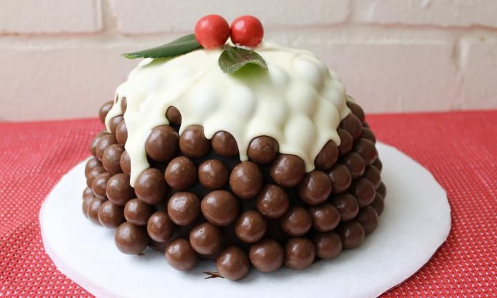 a white plate topped with a cake covered in chocolate candies and frosted cherries