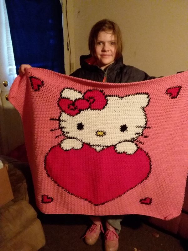 a woman is holding up a knitted blanket with a hello kitty design on it