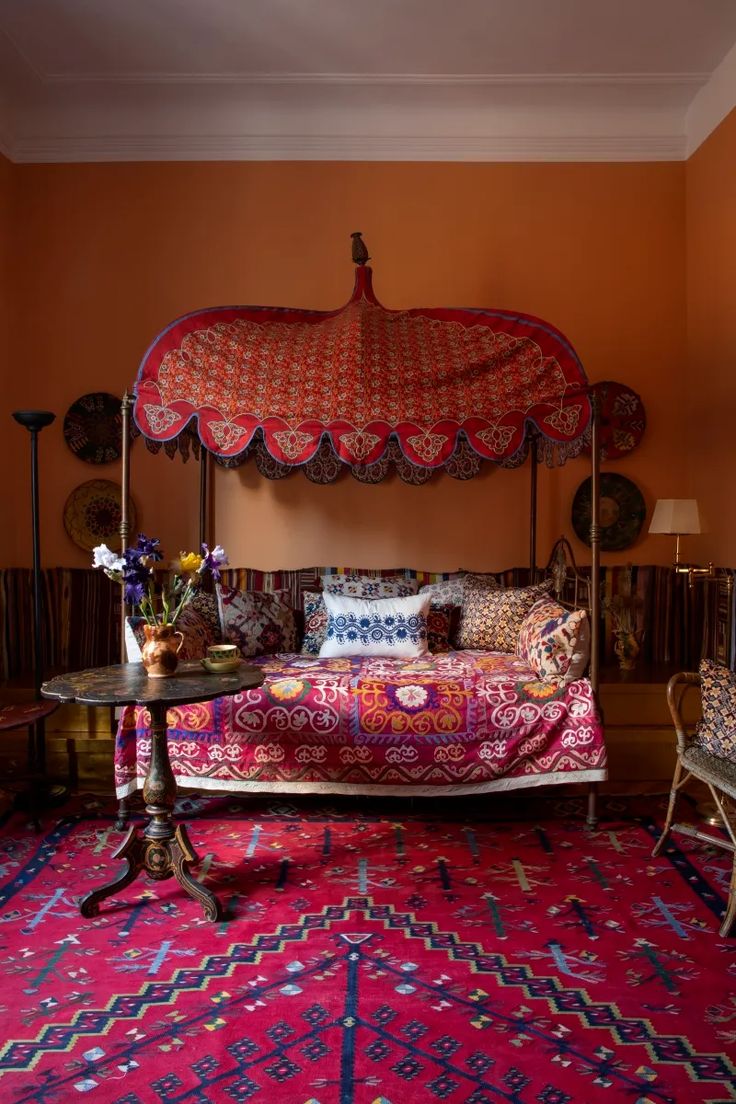 a canopy bed sitting on top of a pink rug next to a table and chairs