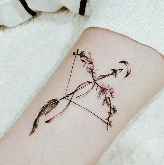 an arrow tattoo with pink flowers on the arm