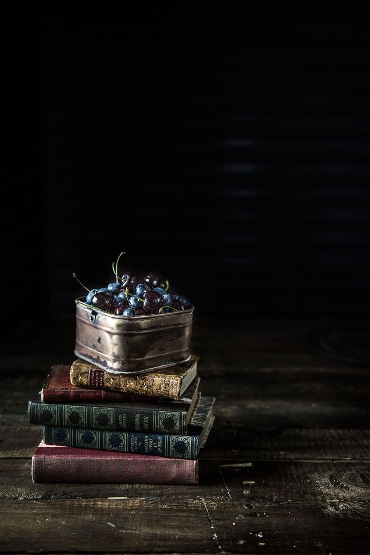 three books stacked on top of each other in front of a metal container filled with berries