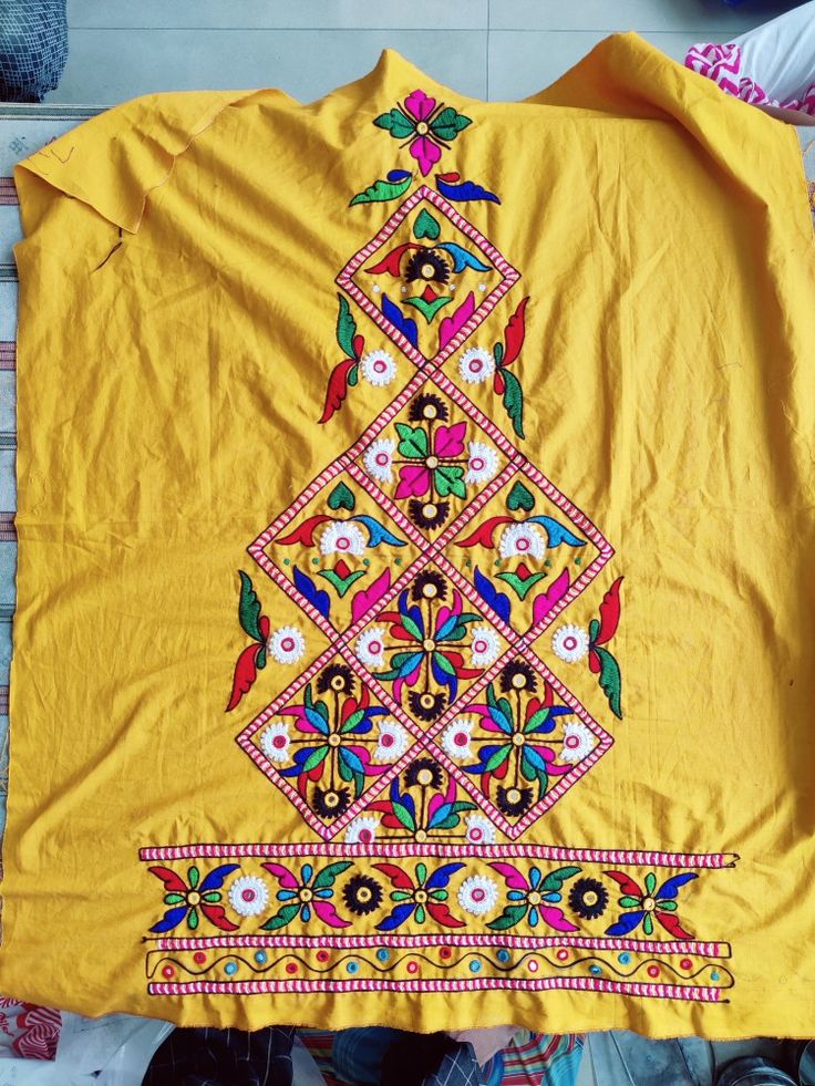 a yellow shirt with an embroidered tree on the front and bottom, sitting on a floor