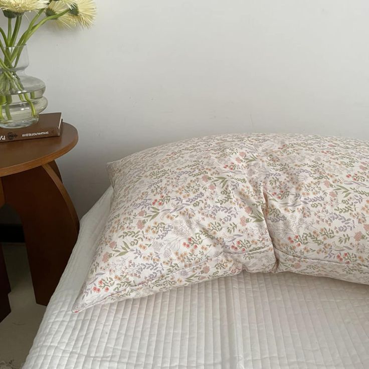 a bed with a white comforter and flowers in a vase on the side table