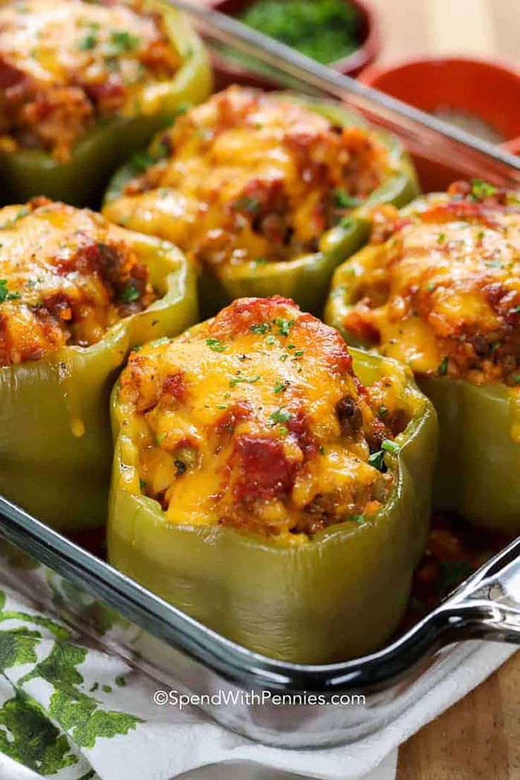 stuffed bell peppers in a casserole dish with cheese and seasoning on top